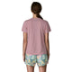 En person med langt brunt hår i en lav hestehale står med ryggen til kameraet iført Patagonia Capilene Cool Ultra Shirt til kvinder i Light Violet - Quiet Violet X-Dye og pastelfarvede shorts med tryk.