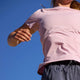 En person i Patagonia Capilene Cool Ultra Shirt, Dame, Light Violet - Quiet Violet X-Dye og mørke shorts ses nedefra mod en blå himmel, med hovedet delvist ude af billedet og den ene arm løftet.