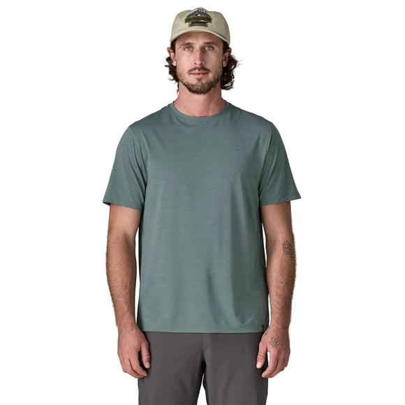 En mand med bølget brunt hår, overskæg og skæg er iført en beige baseballkasket, grå bukser og en Patagonia Capilene Cool Ultra Shirt, Herre, Blue Sage - Light Blue Sage X-Dye, mens han står på en hvid baggrund.