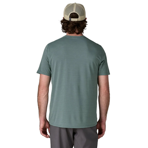 En mand står med ryggen til kameraet iført en Patagonia Capilene Cool Ultra Shirt, Herre, Blue Sage - Light Blue Sage X-Dye, sammen med grå shorts og en beige mesh-back cap på en almindelig hvid baggrund.