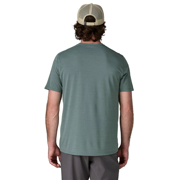 En mand står med ryggen til kameraet iført en Patagonia Capilene Cool Ultra Shirt, Herre, Blue Sage - Light Blue Sage X-Dye, sammen med grå shorts og en beige mesh-back cap på en almindelig hvid baggrund.
