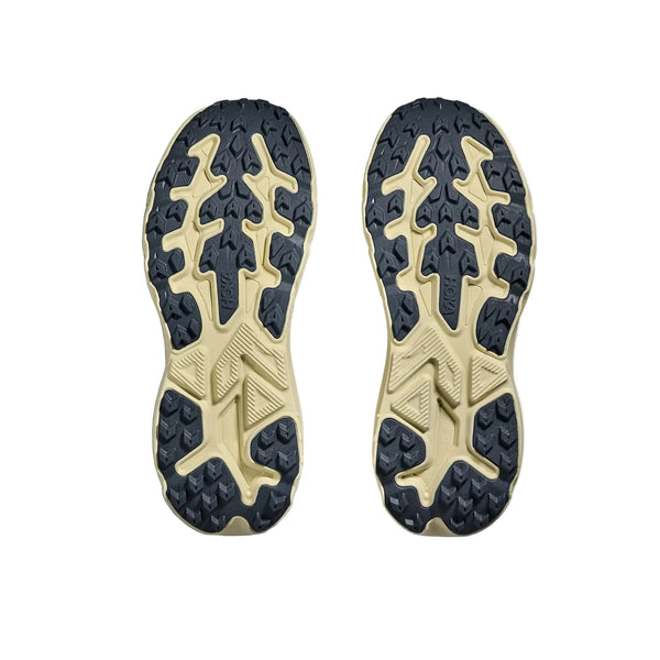 To Hoka Challenger 8 Herre-såler i Faded Navy/Pampass Grass er vist side om side, vendt opad. Deres beige og sorte robuste mønstre giver et godt greb - ideelt som herre løbesko eller trailsko. Baggrunden er hvid.