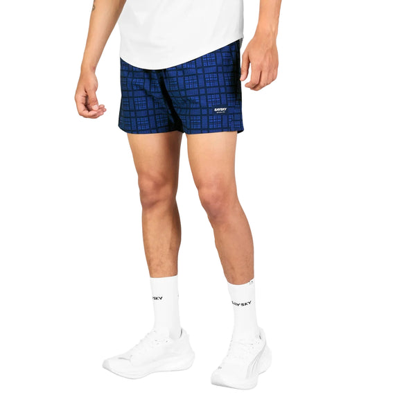 Der vises et billede af en person fra livet og ned, iført Saysky Checker Pace Shorts 5″ til herre i farven Blue Checker, kombineret med en hvid skjorte, hvide sokker og sneakers på en hvid baggrund. Fokus er på disse stilfulde funktionsshorts fra Saysky.