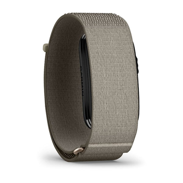 Et armbånd i stoffet »French Grey« med en rektangulær sort enhed, hvor Garmin-logoet er delvist synligt på siden, vist i et skråt sidebillede på en hvid baggrund. Garmin Cirqa Smart Band i farven »French Grey« kombinerer et elegant design med avancerede søvnmålingsfunktioner og fungerer som et aktivitetsarmbånd.
