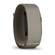 Et armbånd i stoffet »French Grey« med en rektangulær sort enhed, hvor Garmin-logoet er delvist synligt på siden, vist i et skråt sidebillede på en hvid baggrund. Garmin Cirqa Smart Band i farven »French Grey« kombinerer et elegant design med avancerede søvnmålingsfunktioner og fungerer som et aktivitetsarmbånd.