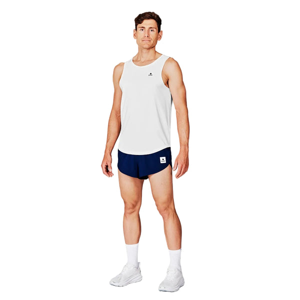 En mand står og kigger fremad iført Saysky Clean Combat Pro Singlet, Herre, White med marineblå løbeshorts, hvide sokker og hvide sportssko. Den enkle hvide baggrund fremhæver dette hurtigtørrende træningstøj, der er ideelt til intens træning.