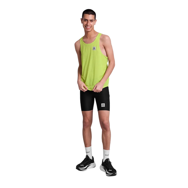 En person står og smiler iført en Saysky Reactive Flow Singlet, Herre, Yellow Logo-en ultralet løbetøj herre-sorte tætsiddende shorts, hvide strømper og sorte sportssko på en almindelig hvid baggrund.