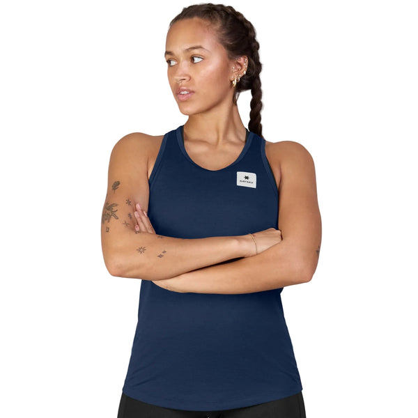 En person med flettet hår og tatoveringer på venstre arm har Saysky Clean Combat Pro Singlet, Dame, Blå, på og kigger til venstre med krydsede arme, mens vedkommende står foran en ensfarvet hvid baggrund.