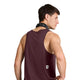 Der ses en mand set bagfra, iført en ærmeløs Saysky Clean Combat Pro Singlet, Herre, i farven Burgundy, med et lille rektangulært mærke nær nederkanten og en sort mønstret bandana om halsen. Han står med den ene hånd på hoften, hvilket fremhæver det eksklusive DELTAPEAK Carat-stof, der gør denne singlet ideel til aktive mænd.