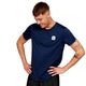 En mand med kort brunt hår og synlige tatoveringer på armene bærer en marineblå Saysky Clean Combat Pro T-shirt, Herre, Blue med et lille hvidt logo på brystet. Han står med hænderne på hofterne, kigger ned og smiler.