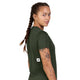 En person med en lang fletning og synlige tatoveringer på armene har en mørkegrøn Saysky Clean Combat Pro-T-shirt til kvinder på og kigger over skulderen. Denne åndbare trænings-T-shirt har på ryggen et lille rektangulært mærke med en sort stjerne på hvid baggrund.