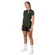 En person står med ansigtet vendt fremad iført en Saysky Clean Combat Pro T-shirt, Dame, i grøn, sammen med sorte shorts, hvide sokker og hvide sneakers. Baggrunden er helt hvid. Personen har synlige tatoveringer på låret og underbenet.