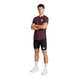 En person står med ansigtet fremad og armene over kors, iført en Saysky Clean Combat Pro T-shirt, Herre, Burgundy, kombineret med sorte shorts, hvide strømper og hvide sneakers. Den åndbare løbetrøje fra Saysky er både let og hurtigtørrende, hvilket gør den ideel til aktiv brug. Baggrunden er ensfarvet hvid.