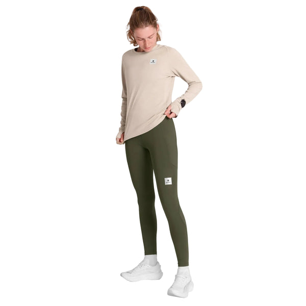 En person iført en beige Clean Flow-langærmet trøje, olivengrønne leggings og hvide løbesko.