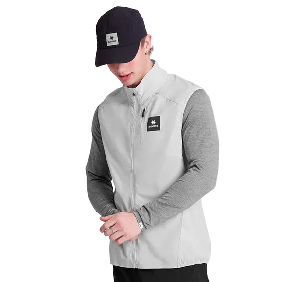 En mand i Saysky Clean Pace Flex Vest, Herre, Grey-light gray zip-up-over en langærmet grå skjorte og mørk kasket med firkantet logo står på en hvid baggrund og kigger ned med let knyttede hænder. Ideel til lag-på-lag løbetøj.