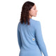 En kvinde med krøllet brunt hår kigger væk iført Saysky Clean Pace Long Sleeve, Dame, Blue - en hurtigtørrende skjorte med en sort stjerne på ryggen. Den ensfarvede hvide baggrund fremhæver den løbetidsklare stil.