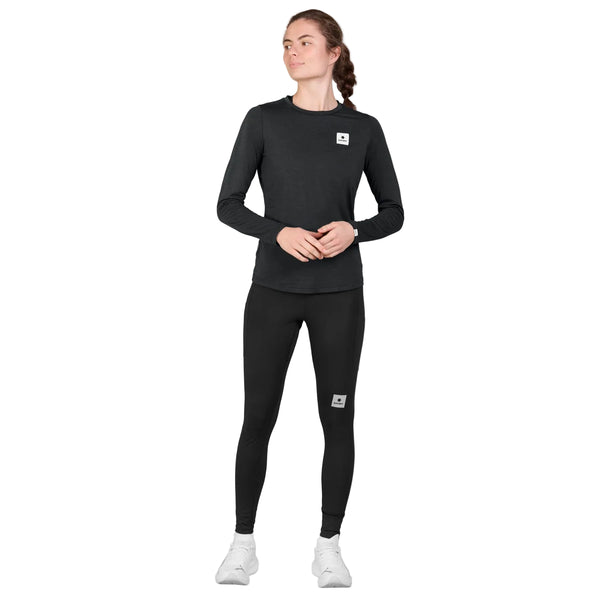 En kvinde iført en sort Clean Pace-langærmet trøje, en Dame-skjorte og sorte leggings samt hvide sneakers.