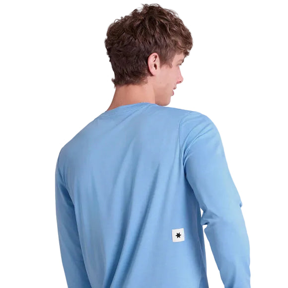 En person med kort, krøllet brunt hår ses bagfra iført Saysky Clean Pace Long Sleeve, Herre, Blue. Skjorten har lange ærmer og et lille hvidt mærke med en sort stjerne nær den nederste kant. Baggrunden er helt hvid.