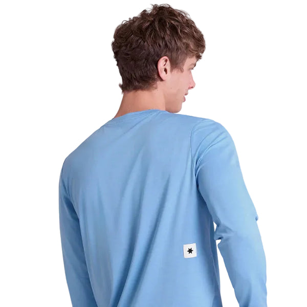 En person med kort, krøllet brunt hår ses bagfra iført Saysky Clean Pace Long Sleeve, Herre, Blue. Skjorten har lange ærmer og et lille hvidt mærke med en sort stjerne nær den nederste kant. Baggrunden er helt hvid.