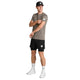 En mand iført en Saysky Clean Pace T-shirt, herre, taupe, kombineret med sorte shorts, hvide sokker og hvide sneakers står vendt mod venstre. Han bærer en sort kasket og rører ved sin ærme, mens han har et neutralt udtryk i ansigtet. Hvert stykke tøj er forsynet med det karakteristiske lille rektangulære logo. Den hurtigtørrende Clean Pace T-shirt fra Saysky sikrer komfort under enhver aktivitet.
