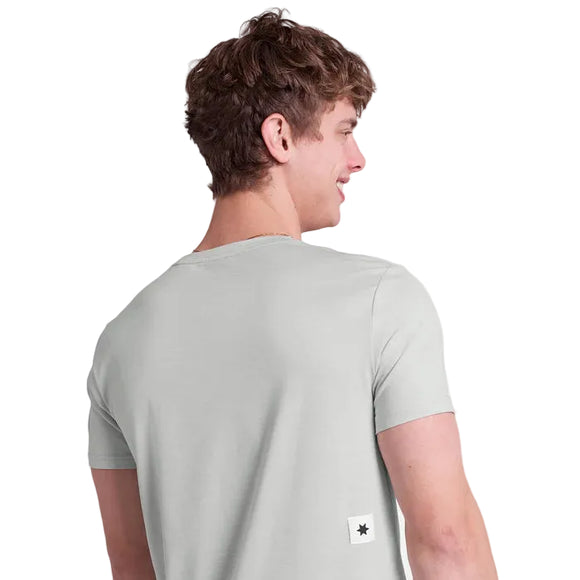 En person med kort, krøllet brunt hår ses bagfra iført en lysegrå Saysky Clean Pace T-shirt, Herre. Et lille hvidt mærke med en sort stjerne ses nær den nederste kant i højre side.