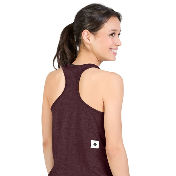 En kvinde med mørkt hår sat op i en hestehale har en Saysky W Clean Combat Pro Singlet, Dame, Burgundy på – en hurtigtørrende, ærmeløs, maroon racerback-tanktop med et lille hvidt mærke med en sort stjerne nederst på ryggen. Hun står med ryggen til kameraet og smiler foran en hvid baggrund.