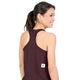 En kvinde med mørkt hår sat op i en hestehale har en Saysky W Clean Combat Pro Singlet, Dame, Burgundy på – en hurtigtørrende, ærmeløs, maroon racerback-tanktop med et lille hvidt mærke med en sort stjerne nederst på ryggen. Hun står med ryggen til kameraet og smiler foran en hvid baggrund.