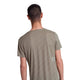 En person med kort mørkt hår ses bagfra iført en Saysky Reactive Flow T-shirt, Herre, Dark Beige Logo, med et lille rektangulært mærke nederst på ryggen mod en almindelig hvid baggrund.