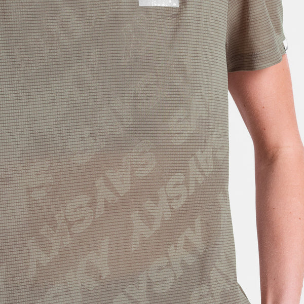 Nærbillede af en person iført Saysky Reactive Flow T-shirt til mænd med et diskret gittermønster, "SKY" med store, svage bogstaver og et mørkebeige logo. Kun den ene arm og en del af overkroppen er vist.