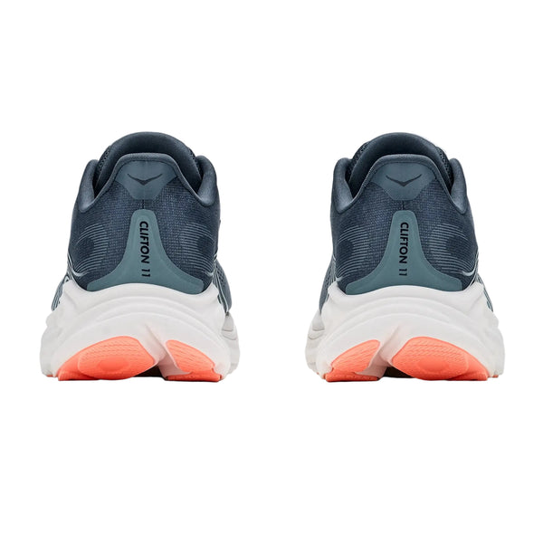 Et par Hoka Clifton 11-damesko i farven Faded Navy / Glimmering Blue ses set bagfra, hvor teksten »Clifton 11« på hælene fremhæves. Sålerne giver maksimal støddæmpning og har et overvejende hvidt design med orange sektioner ved hæl- og tåområdet. Baggrunden er ensfarvet hvid.
