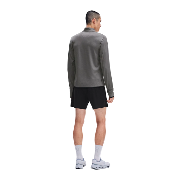 En mand står med ryggen til kameraet iført en grå On Climate Shirt 3, Herre, Ember – en perfekt løbetrøje til mænd i koldt vejr – sammen med sorte shorts, hvide sokker og grå løbesko. Han står foran en ensfarvet hvid baggrund.