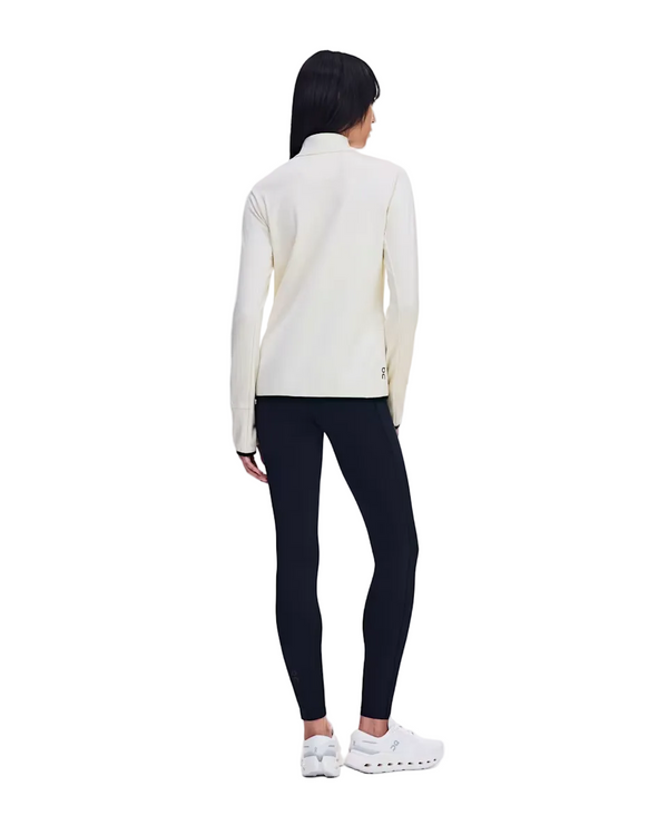 En person med langt hår står med ryggen til kameraet foran en ensfarvet hvid baggrund og har en On Climate Shirt Dame Hare på, kombineret med sorte leggings og hvide sportssko.