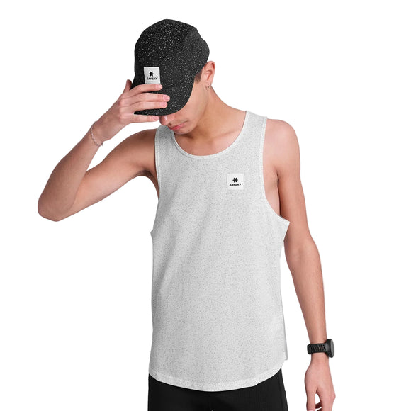 En person i hvidprikket tanktop og Saysky Combat Cap, Unisex, Black Universe, begge med et lille firkantet logo, vipper kasketten nedad med den ene hånd. Personen bærer også et armbåndsur.