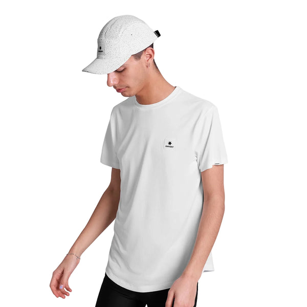 En person iført Saysky Combat Cap, Unisex, White Universe og en almindelig hvid t-shirt med et lille sort logo står på en hvid baggrund og kigger ned og til siden.