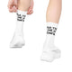 Der ses to ben iført hvide Saysky Combat High Socks, unisex, med påskriften »For The Love Of Running«, kombineret med hvide sportssko. Strømperne har sort tekst, hvor der står »FOR THE LOVE OF RUNNING«, hvilket fremhæver deres karakteristiske stil. Den ene hånd er i færd med at rette kanten på den venstre strømpe. Baggrunden er ensfarvet hvid.