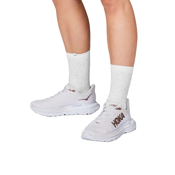 En person iført Saysky Reflective Combat High Socks i hvid og hvide HOKA-løbesko med brunt branding står på en hvid baggrund, hvor kun underben og fødder er synlige.