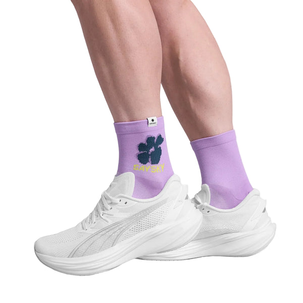 En person er iført Sayskys unisex Combat Quarter Socks i lilla - designet til performance-komfort og en ultra-åndbar følelse - sammen med hvide sportssko på en hvid baggrund.