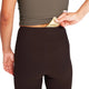 En kvinde i Saysky Combat+ Rib Long Tights, Dame, Coffee og en olivengrøn top stikker en guldpakke ned i den skjulte linningslomme bag på sine leggings.