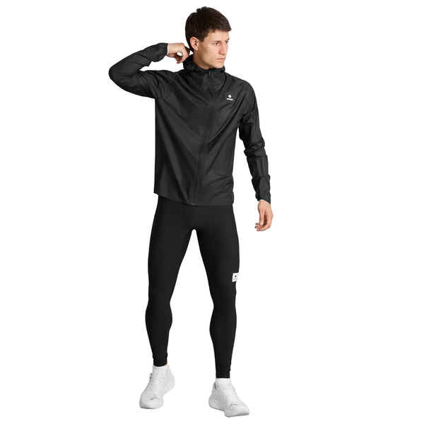 En mand iført en sort sportsjakke og Saysky Combat+ Rib Long Tights, Herre, Sort står vendt til siden med højre hånd tæt på kraven. Han har hvide sneakers på og kigger mod venstre. Løbetightsene til herre fra Saysky er fremstillet af åndbart ribstof, hvilket sikrer komfort under enhver aktivitet. Baggrunden er ensfarvet hvid.