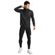 En mand iført en sort sportsjakke og Saysky Combat+ Rib Long Tights, Herre, Sort står vendt til siden med højre hånd tæt på kraven. Han har hvide sneakers på og kigger mod venstre. Løbetightsene til herre fra Saysky er fremstillet af åndbart ribstof, hvilket sikrer komfort under enhver aktivitet. Baggrunden er ensfarvet hvid.