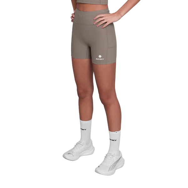 En person er iført taupe Saysky Combat+ Rib Running Short Tights 4" og en matchende sports-bh med hvidt logo, sammen med hvide strømper og sportssko. Hænderne er på hofterne; hovedet er ikke synligt.