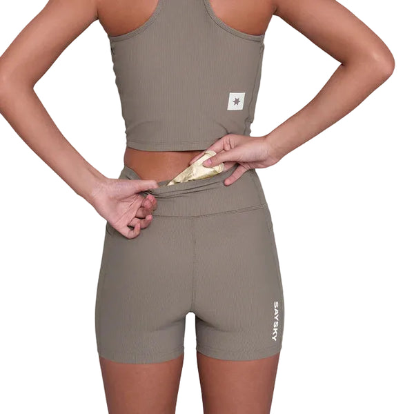 Person in åndbart træningstøj fra Saysky iført Combat+ Rib Running Short Tights 4" i taupe, står med ryggen til og løfter linningen for at vise en skjult lomme med et item. Logo og mærker er synlige på tøjet.