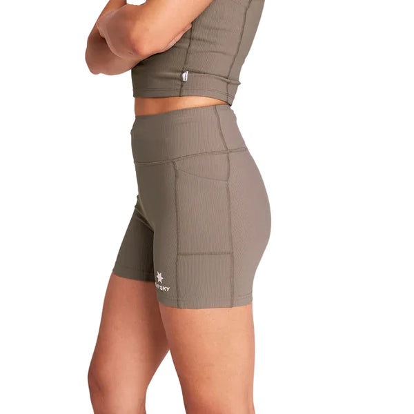 En person i en matchende olivengrøn crop top og Saysky Combat+ Rib Running Short Tights 4" for women i taupe står med armene over kors. Strømpebukserne har en sidelomme, et lille logo nær kanten og en hvid baggrund.