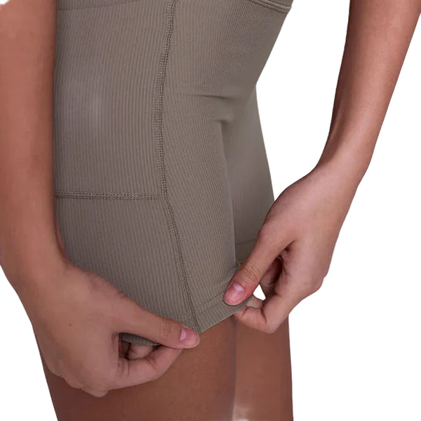 Her ses en kvinde, der fra taljen og ned justerer kanten på Saysky Combat+ Rib Running Short Tights 4" i taupe. Den åndbare træningstøj skiller sig ud mod en almindelig hvid baggrund.