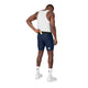 En mand iført en hvid tanktop og et par Saysky Combat+ Rib Short Tights 8″ (Herre, blå) lægger et kort eller en seddel i baglommen. Han har hvide sokker og sneakers på og står med ryggen til kameraet foran en ensfarvet hvid baggrund.