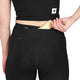 En person, der har Saysky Combat+ Short Tights 7″, Dame, Sort på – fremstillet af genanvendt polyester – lægger en genstand i guldindpakning, muligvis en snack eller en energibar, ned i baglommen med lynlås i linningen. Personens overkrop og hånd er synlige.