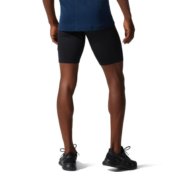 En person står med ryggen til og er iført en blå trøje, Asics Core Sprinter Short Tights Herre i sort og sorte sportssko. Kun underkroppen og benene er synlige, med armene afslappet i siden.