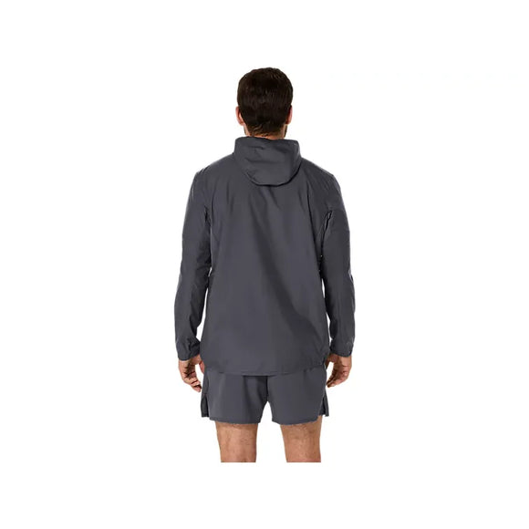 En person står med ryggen til kameraet, iført en mørkegrå Asics Core Jacket, Herre, i farven Carrier Grey samt matchende shorts. Denne vandafvisende jakke fra Asics er ideel som en løbejakke til mænd for dem, der ønsker både stil og funktionalitet. Baggrunden er ensfarvet hvid.