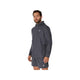 En mand har en Carrier Grey ASICS Core Jacket, Herre — en vandafvisende løbejakke til mænd — på sammen med et par matchende shorts. Begge dele har et lille hvidt ASICS-logo på venstre side. Jakken skiller sig ud mod den ensfarvede hvide baggrund, mens han kigger let til venstre.