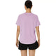En kvinde ses bagfra iført en tåget, lilla Core Ss Top fra Asics, der er lavet af hurtigtørrende stof, samt sorte shorts. Hendes hår er sat op i en knold, armene hænger afslappet ned langs siden, og hun står foran en ensfarvet hvid baggrund.
